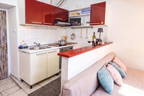 A compact kitchen with white cabinets, a red countertop, and a built-in oven. - Ema Studio on the Main Promenade (Koper)