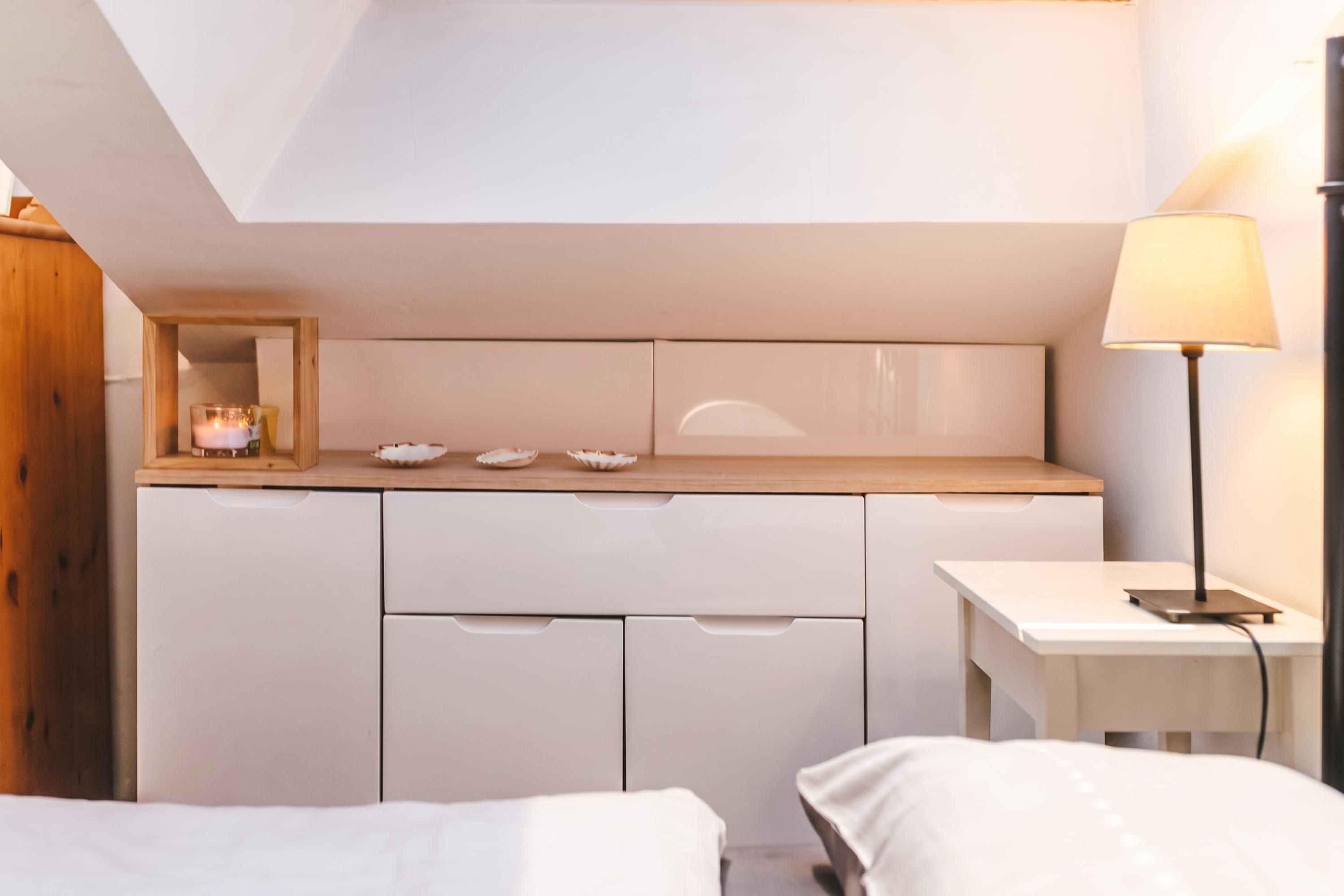 A modern bedroom with a skylight, a bedside table with a lamp, and a small shelf with decorative items.