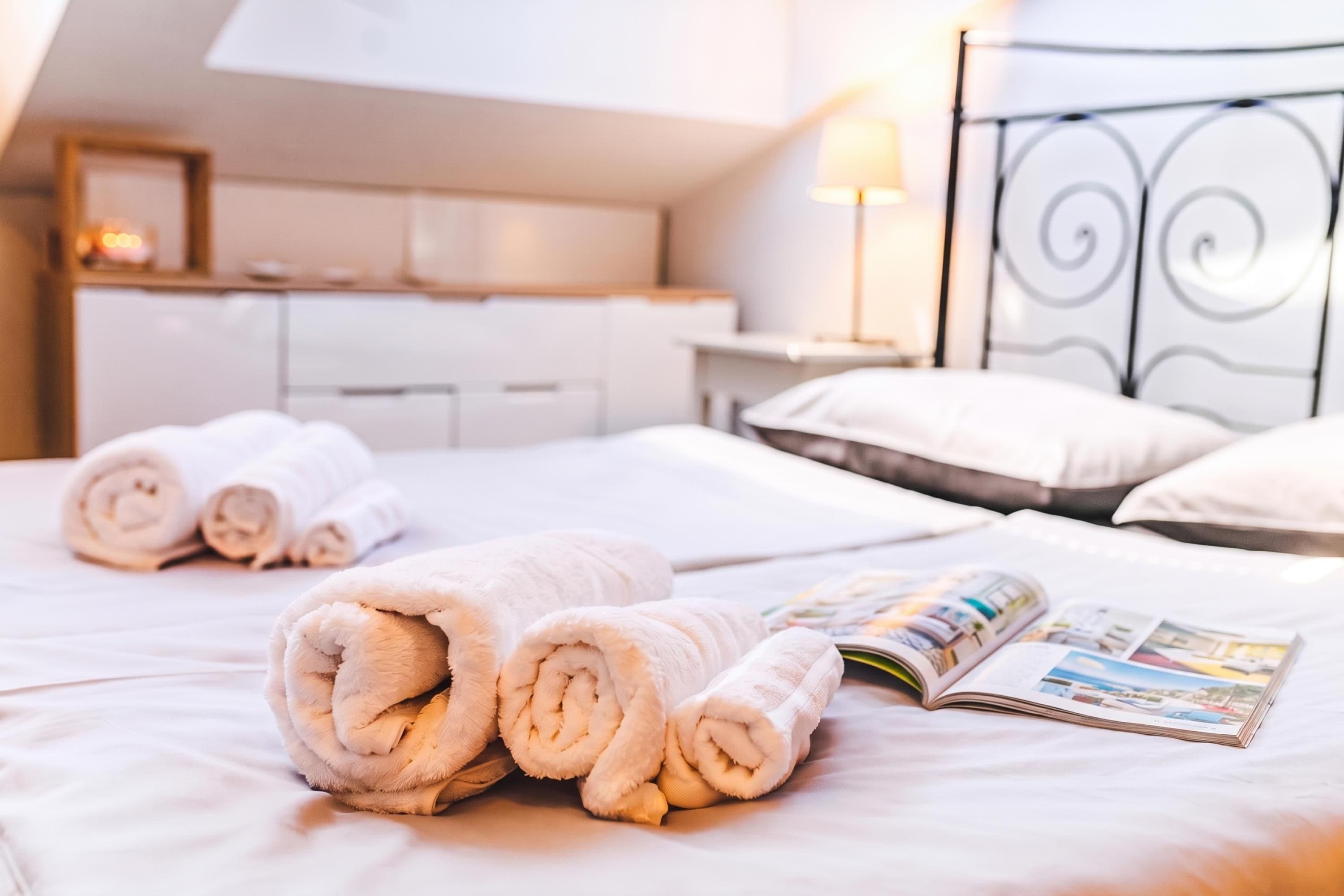 A neatly made bed with rolled towels and an open magazine.