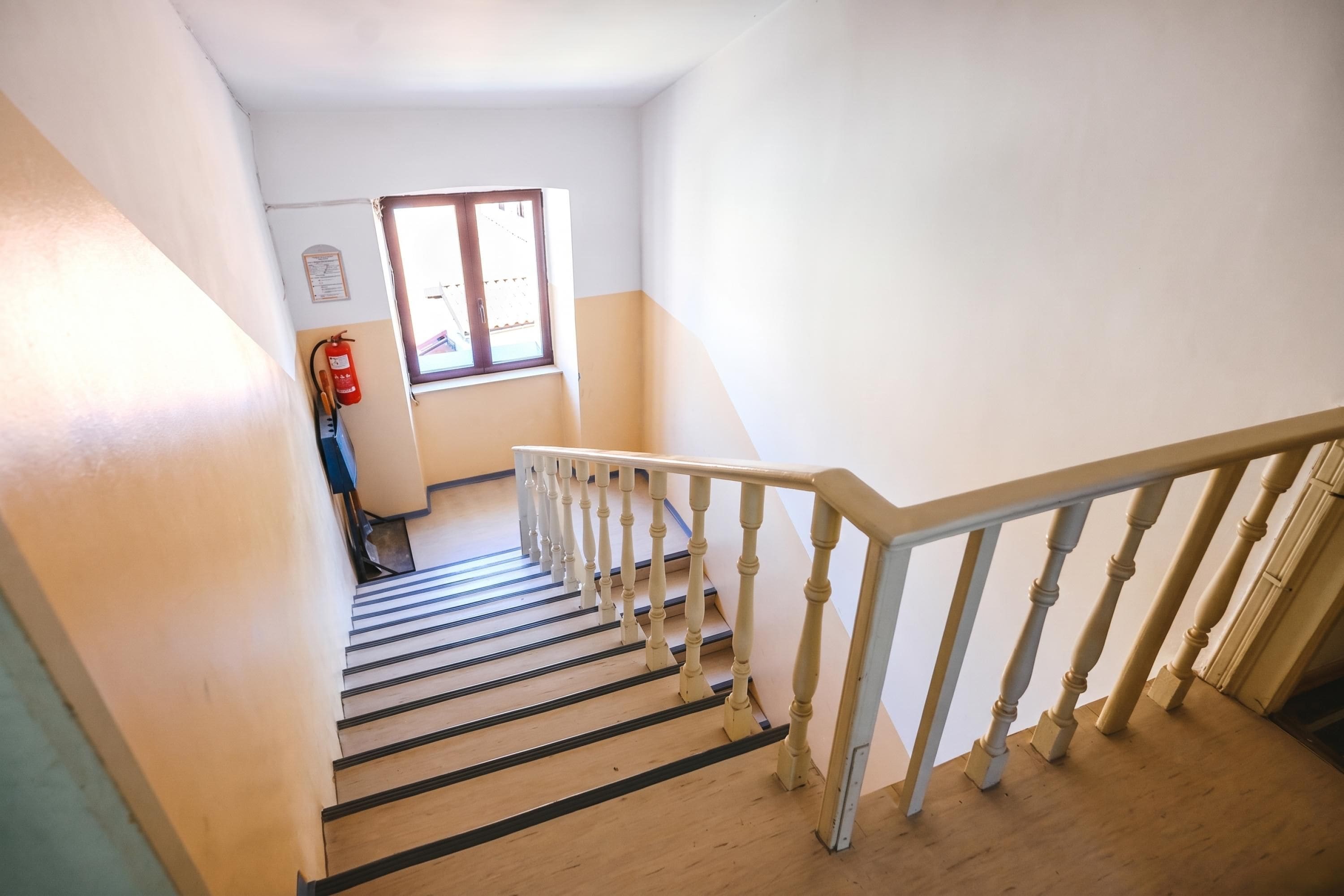 A staircase with wooden steps and white balusters, leading to a landing with a fire extinguisher mounted on the wall.