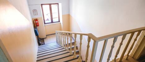 A staircase with wooden steps and white balusters, leading to a landing with a fire extinguisher mounted on the wall.