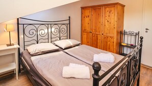 A double bed with a metal frame, two pillows, and a folded towel on each bed. There is a wooden wardrobe and a small shelf with a lamp and a hairbrush. - Ema Studio on the Main Promenade (Koper)