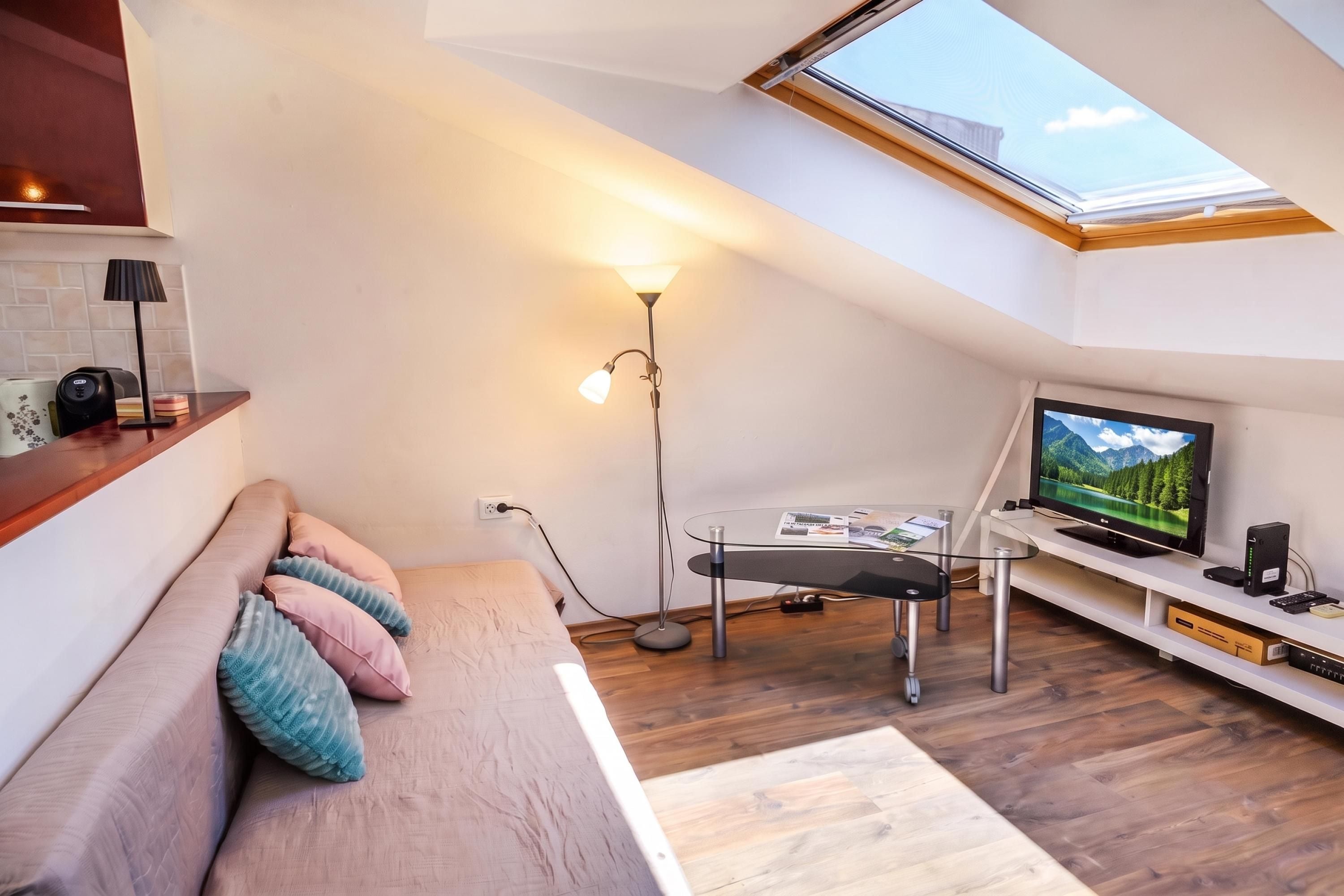 Et moderne loftværelse med ovenlys, en seng med puder, et skrivebord med en computer og et fjernsyn.