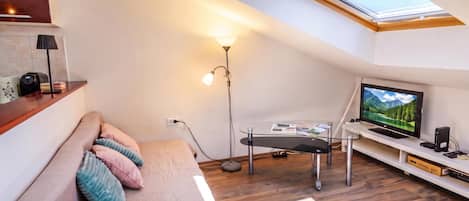 Et moderne loftværelse med ovenlys, en seng med puder, et skrivebord med en computer og et fjernsyn.