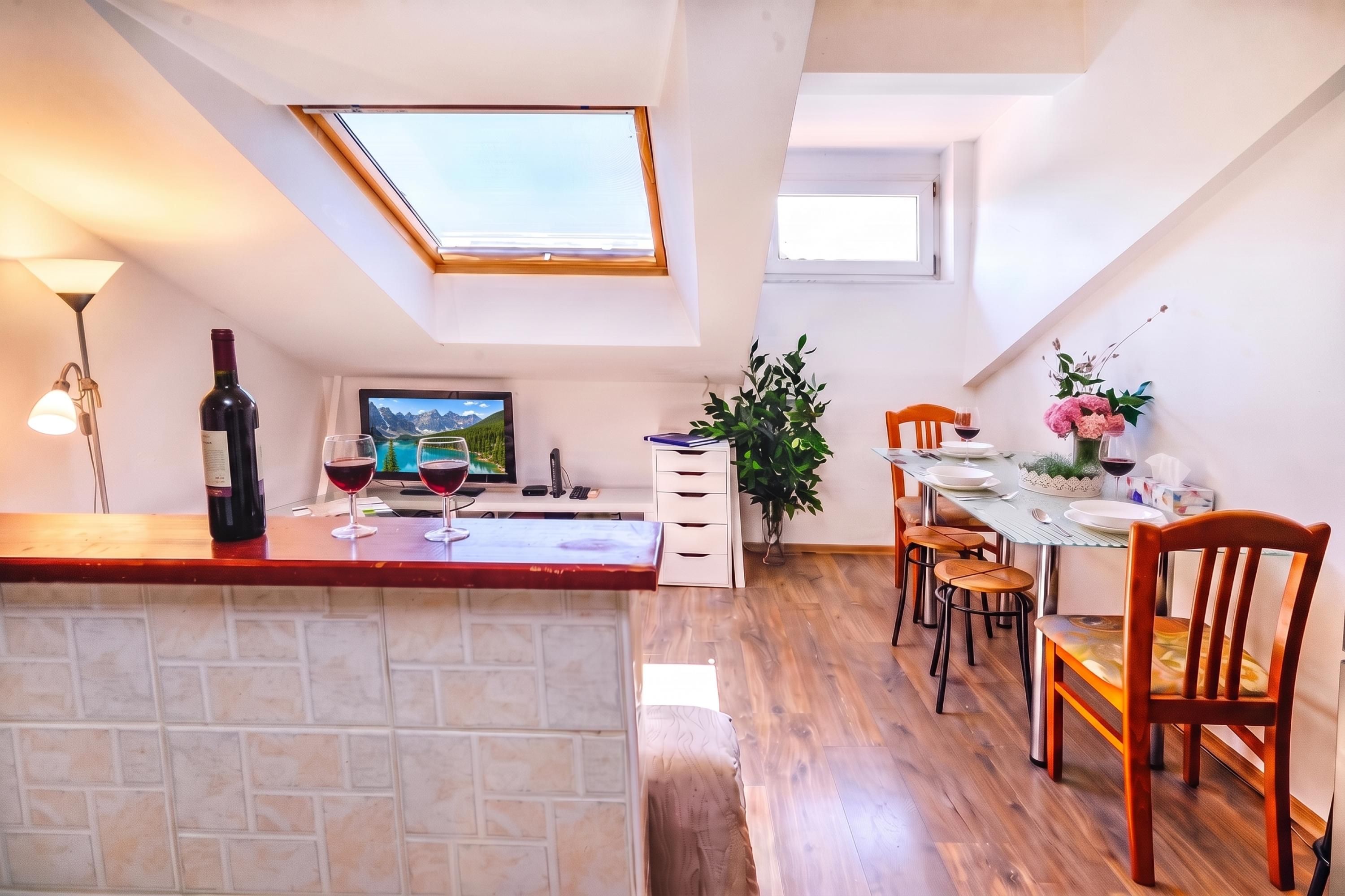Una cocina con comedor, televisor, botella de vino y una planta.
