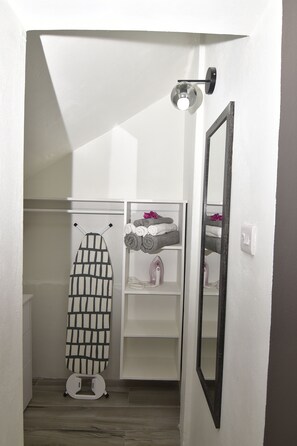 Casa de banho com porta-toalhas, espelho e prateleira com toalhas e um ferro de passar roupa.