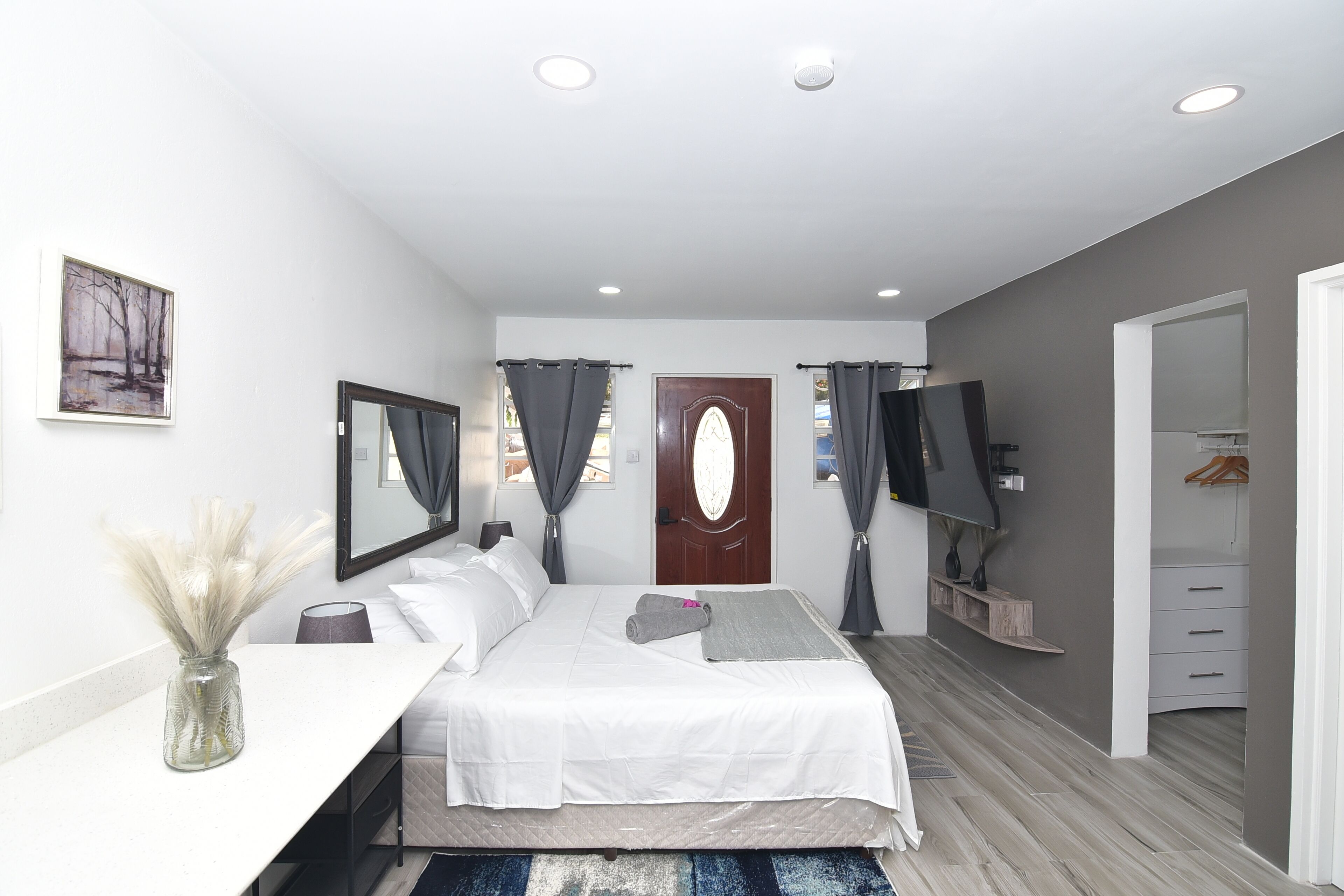 Een moderne slaapkamer met een bed, nachtkastje, spiegel, kunstwerk en een televisie.