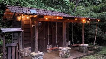 A rustic wooden cabin with a porch, stone steps, and hanging lights.