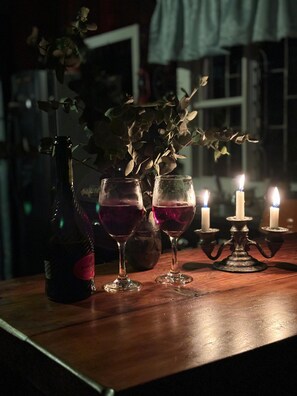 Una mesa tenuemente iluminada con una botella, dos vasos de líquido rojo y un candelabro con velas encendidas.