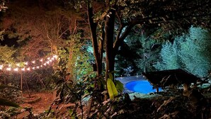 A nighttime outdoor setting with a pool, string lights, and a thatched structure. - Family & Pet friendly•Nestled in the forest•Trails•Waterfalls 13 km away•8 beds• (Luisa)