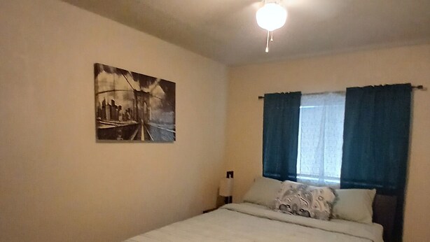 A bedroom with a bed, a ceiling fan, a window with curtains, and a wall-mounted painting. - Charming 3-bedroom house in peaceful San Antonio near military bases (San Antonio)