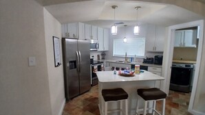 A compact kitchen with a refrigerator, microwave, and a small island with stools. - Charming 3-bedroom house in peaceful San Antonio near military bases (San Antonio)
