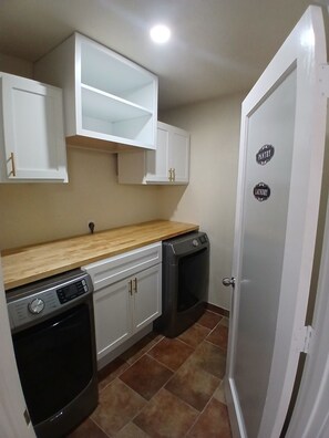 A compact kitchen with white cabinets, a wooden countertop, a dishwasher, and a washing machine.