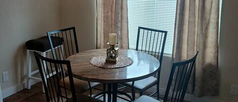 Un coin repas avec une table ronde, six chaises, un centre de table décoré d’une bougie et un lustre.