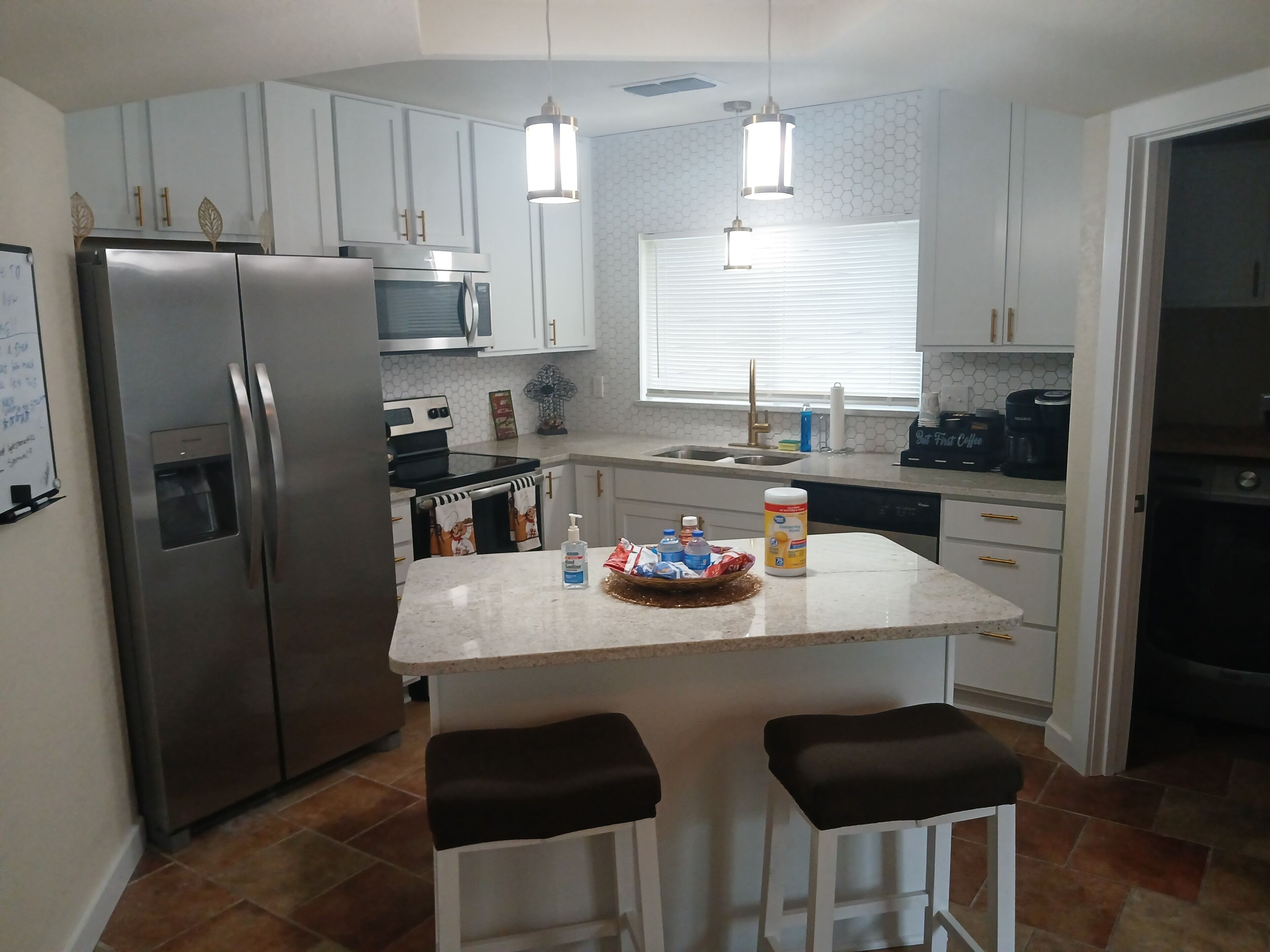 Una cocina moderna con un refrigerador de acero inoxidable, un microondas y una cafetera. Hay dos taburetes de bar y una pequeña isla con una cesta.