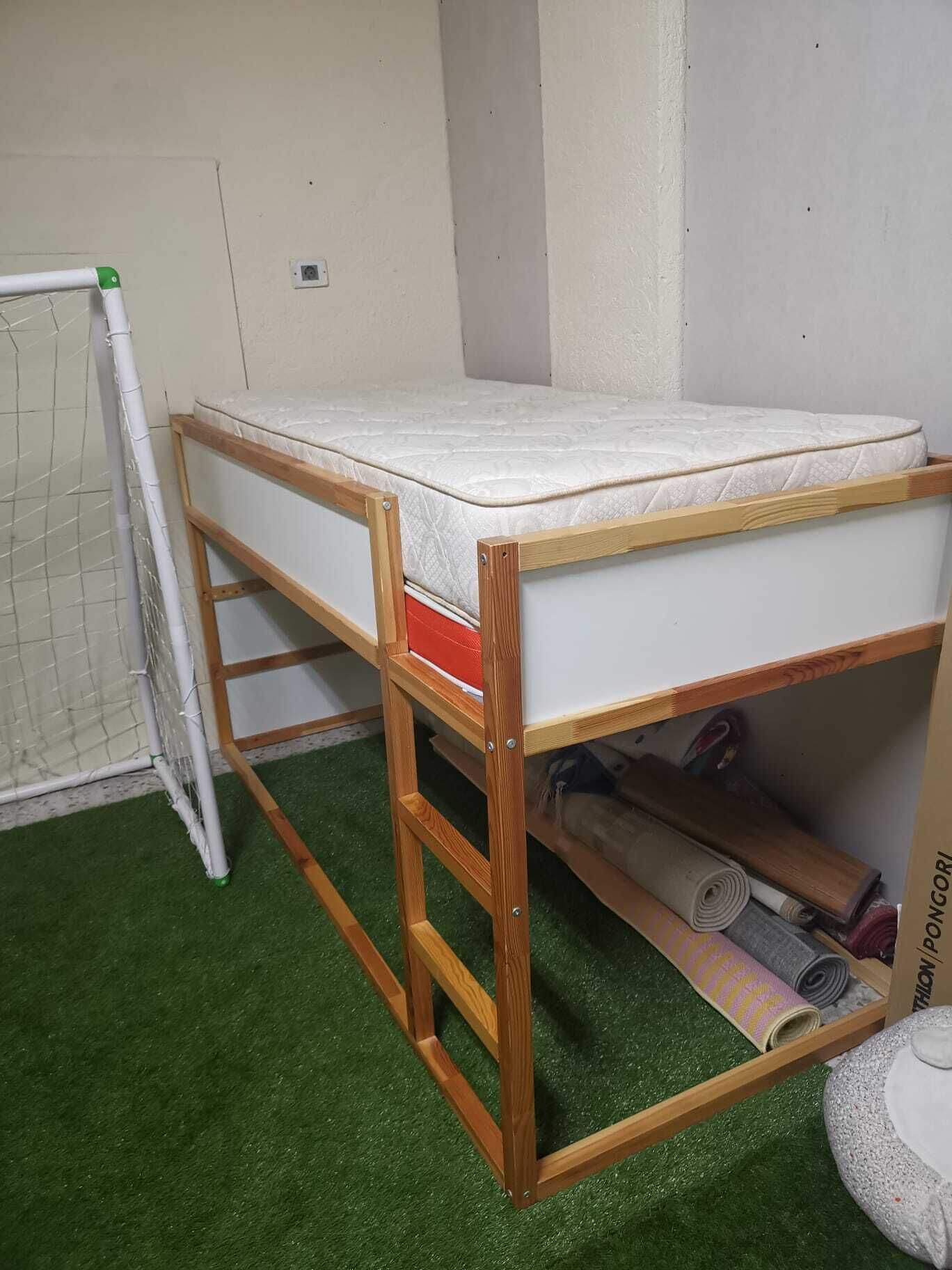Un lit superposé avec un matelas, une structure en bois et une étagère de rangement en dessous.