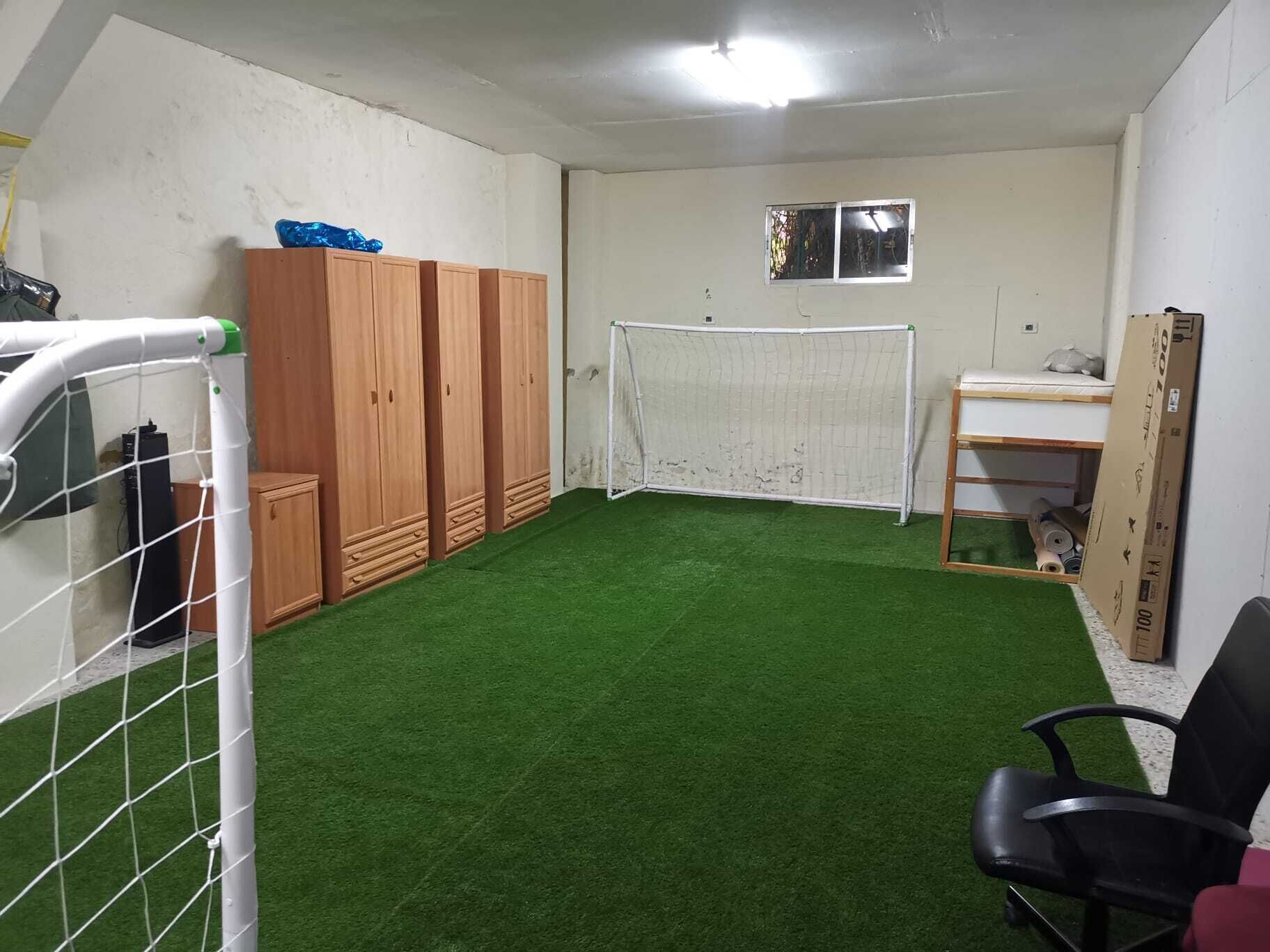 Una stanza con erba sintetica, una porta da calcio, mobili in legno e una scrivania con uno specchio.