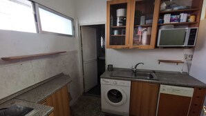 Cocina compacta con lavadora, microondas y armarios de madera.