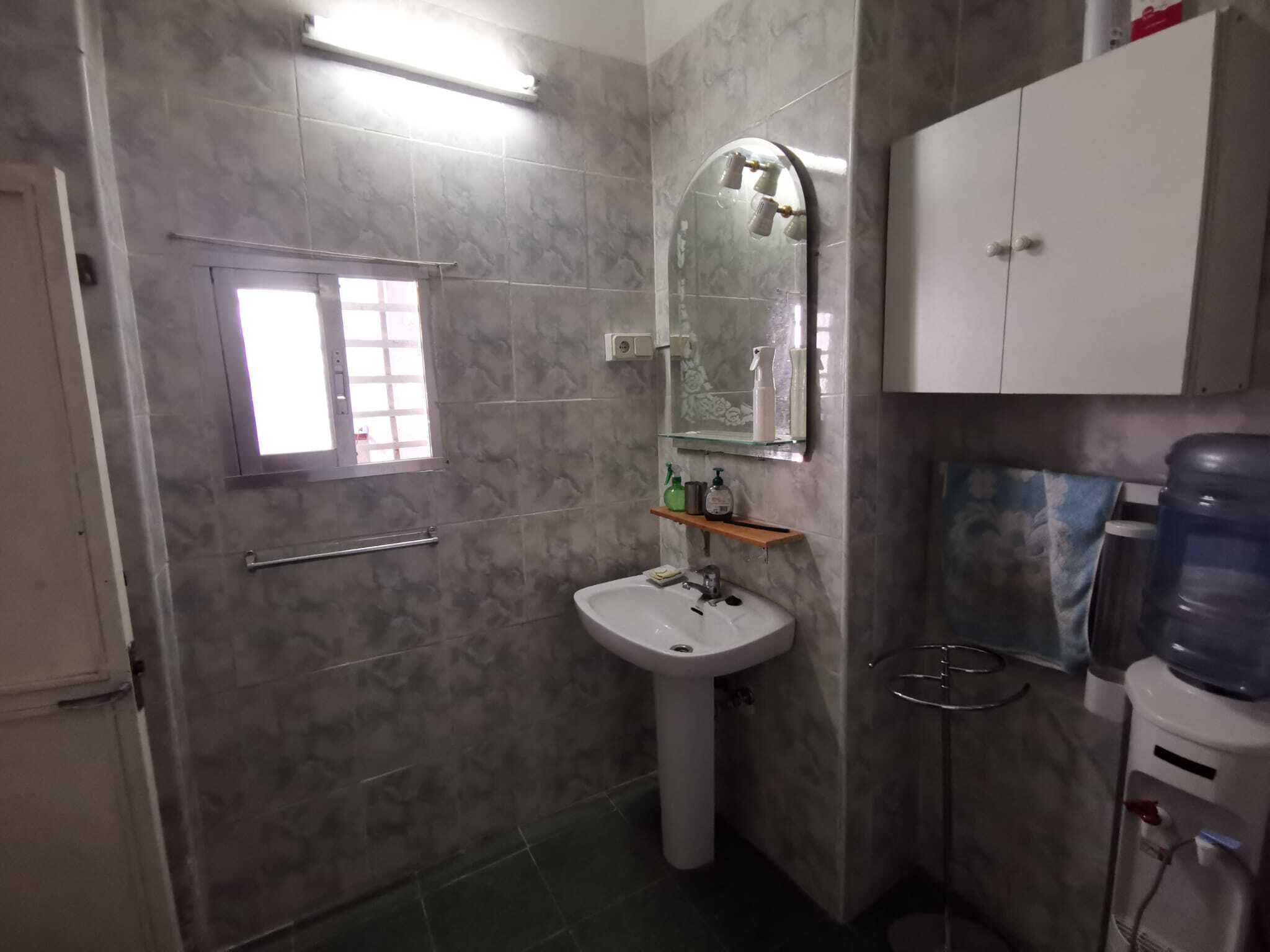 Un bagno con un lavabo su piedistallo, uno specchio, un armadietto, una finestra e un erogatore d'acqua.