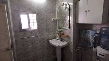 Un bagno con un lavabo su piedistallo, uno specchio, un armadietto, una finestra e un erogatore d'acqua.