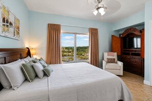A hotel room with a large bed, a chair, a TV, and a view of the outdoors. - Shores of Panama 704- 2BR Gulf View (Sleeps 8) (Panama City Beach)