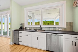 Una cucina moderna con mobili bianchi, una lavastoviglie in acciaio inossidabile e un'ampia finestra vista sul verde.
