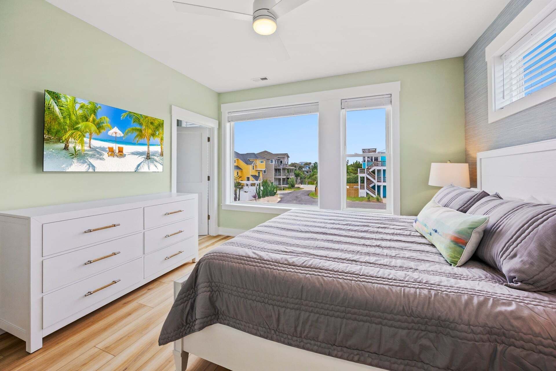 Quarto com cama, cômoda e uma grande janela com vista para casas.