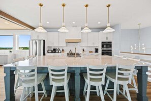A modern kitchen with a large island, white cabinetry, and pendant lighting. - Coastal Bliss - Oceanfront w/ views, pool, hot tub, and easy beach access. (Corolla)