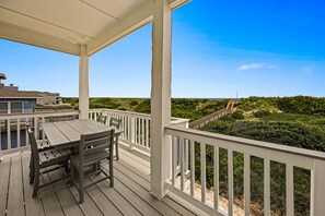 Ein überdachter Außenbereich mit Tisch und Stühlen, mit Blick auf einen Strand, auf dem eine Holztreppe hinabführt.