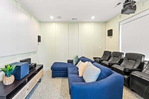 Ein Heimkinozimmer mit einer Eckcouch, einem Flachbildfernseher, einer Soundanlage und einem Projektor.