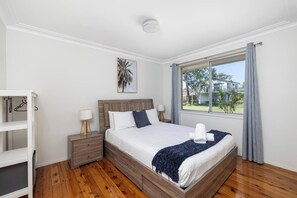 Habitación de hotel con una cama de madera, una mesita de noche, una lámpara, un ventanal con vistas al exterior y un cuadro en la pared.