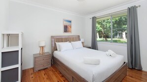 A hotel room with a bed, bedside tables, a window with curtains, and a painting on the wall. - Barefoot Bungalow Walk to Little Beach (Nelson Bay)