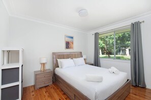 A hotel room with a bed, bedside tables, a window with curtains, and a painting on the wall. - Barefoot Bungalow Walk to Little Beach (Nelson Bay)