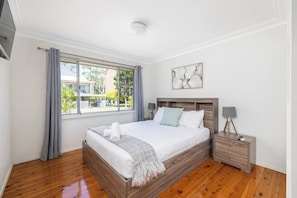 A bedroom with a wooden bed, a nightstand, a lamp, and a window with curtains.