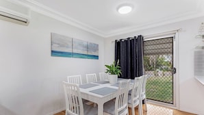 A dining area with a white table, chairs, and a potted plant. - Barefoot Bungalow Walk to Little Beach (Nelson Bay)