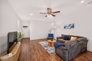 A modern living room with a sofa, a TV, a ceiling fan, and a wooden floor. - Modern Comfort, Prime Location/SeaWorld/Six Flags (San Antonio)