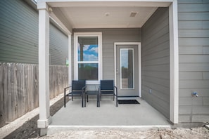 A covered porch with two chairs and a table, a door, and a window with blinds. - Modern Comfort, Prime Location/SeaWorld/Six Flags (San Antonio)