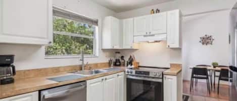 A modern kitchen with white cabinets, a dishwasher, an oven, and a coffee machine.