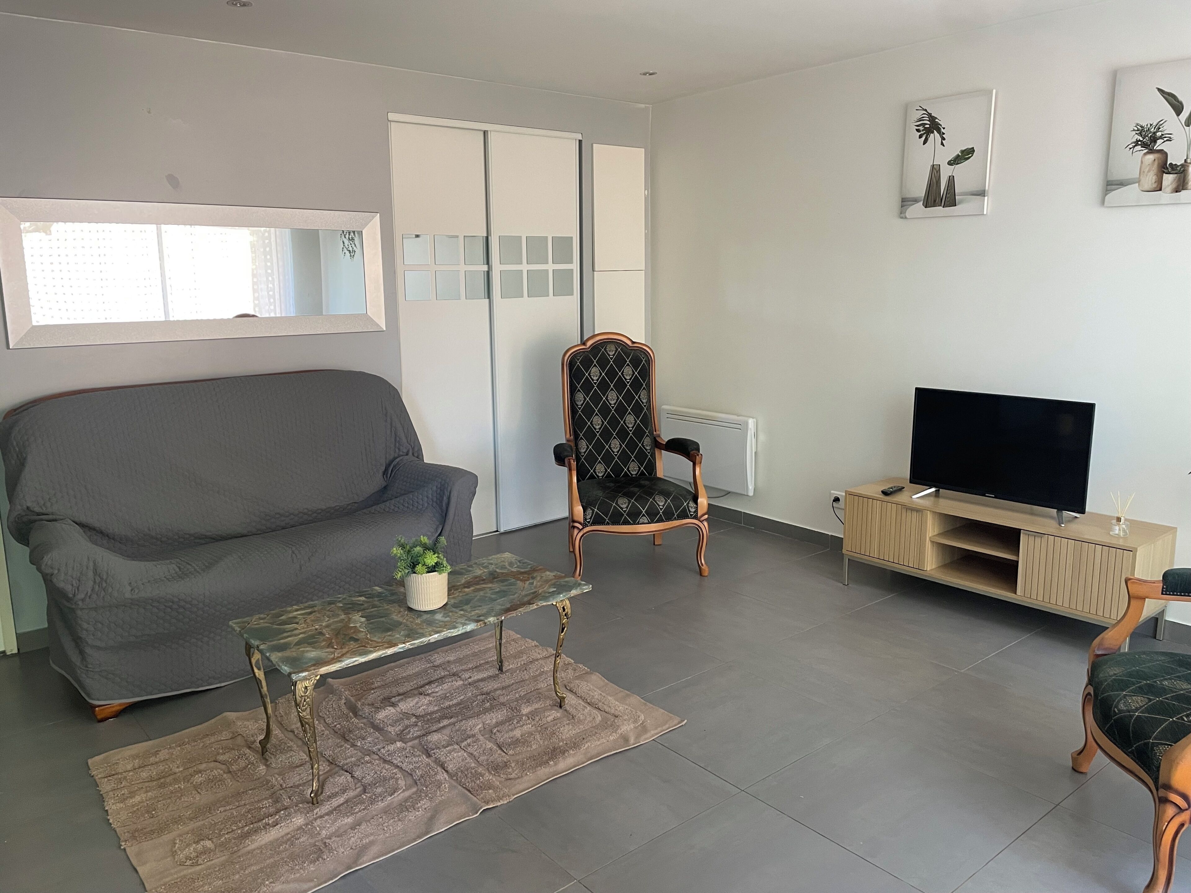 Un salón con un sofá gris, un sillón estampado, una mesa de centro, un mueble para televisor y un radiador.