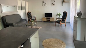 A modern living room with a sofa, two armchairs, a coffee table, a TV, and decorative plants. - 3-room NE apartment on the garden level (Varetz)
