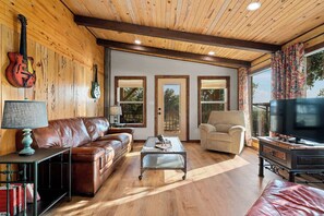 A cozy living room with a leather sofa, a coffee table, and a television. - Luckenbach House, Hot tub, Views! (Fredericksburg)