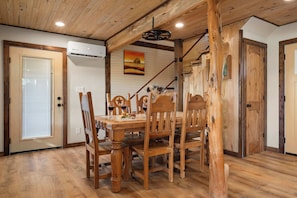 A dining area with a wooden table and chairs, an air conditioning unit, and a painting on the wall. - Luckenbach House, Hot tub, Fire pit, Views! (Fredericksburg)