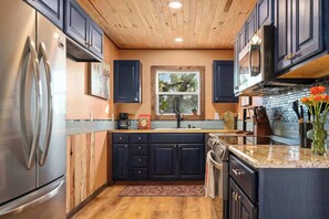 A kitchen with dark cabinets, stainless steel appliances, a window with a view, and a countertop with a vase of flowers. - Luckenbach House, Hot tub, Views! (Fredericksburg)