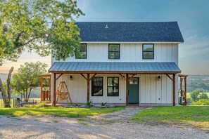 A two-story house with a covered porch, a front door, and a view of the landscape. - Luckenbach House, Hot tub, Views! (Fredericksburg)