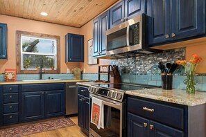 A modern kitchen with dark blue cabinets, stainless steel appliances, and a stone backsplash. - Luckenbach House, Hot tub, Fire pit, Views! (Fredericksburg)