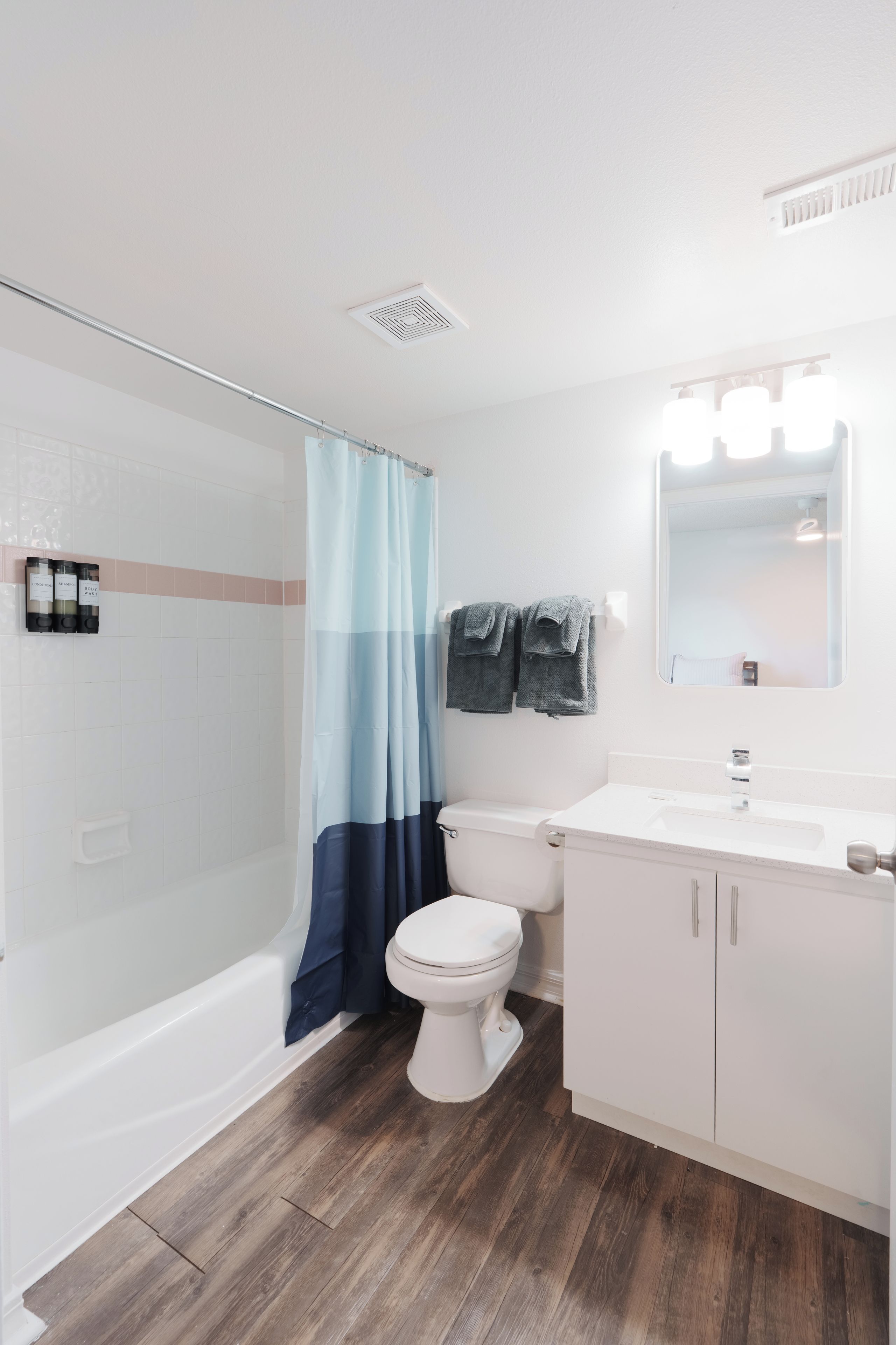 Een badkamer met een wit toilet, een douche met een blauw gordijn en een wastafel met een spiegel.