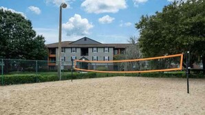 A sandy beach volleyball court with a net, surrounded by a fence and trees. - Mins 2: VA, UF SanteFe U, UF Shands, HCA ,Airport (Gainesville)