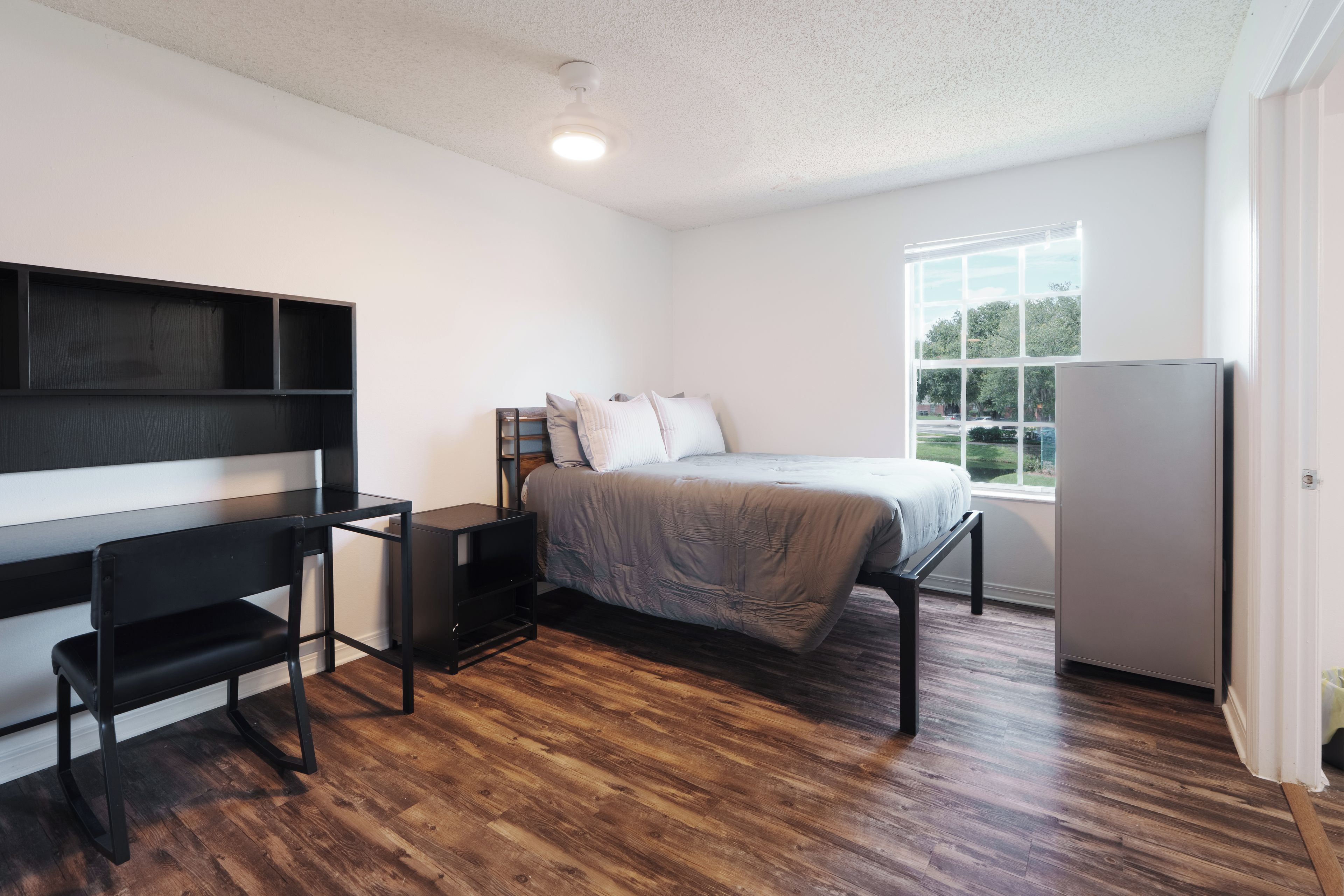 A bedroom with a bed, a desk, and a window.