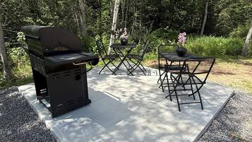 Un espace barbecue extérieur avec une table et des chaises, entouré d’arbres.