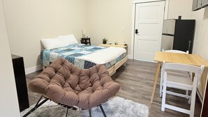 A bedroom with a bed, a chair, a desk, and a door.